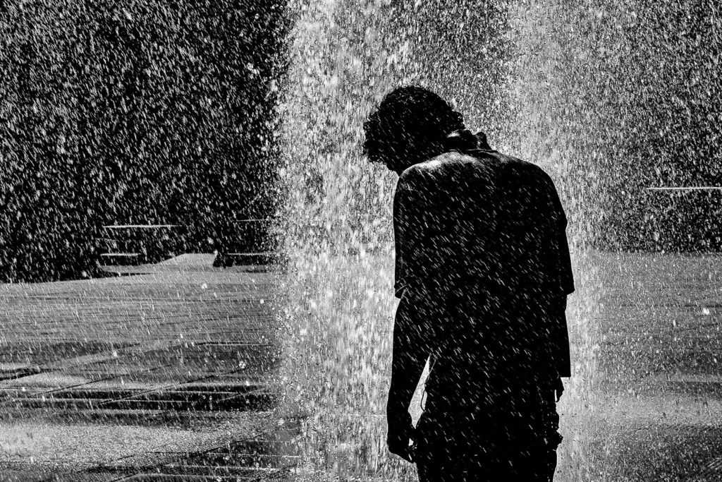 Fotografia em preto e branco de figura humana solitária sob cortina de água na Praça da Estação em Belo Horizonte por Ricardo Laf, chancelada com Reconhecimento Especial na Exposure Photo Gallery.