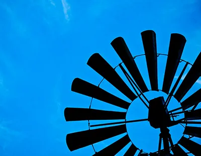 Fotografia em contra-plongée da silhueta das hélices de um moinho de vento destacadas contra o céu azul intenso.