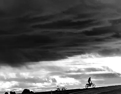 Fotografia em preto e branco com silhueta em movimento sobre uma estrada contra um céu aberto e dramático em Hafnarfjörður, Islândia.
