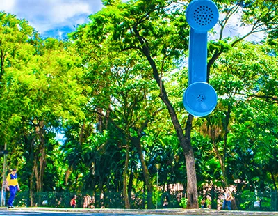 Fotografia urbana de orelhão azul antigo em destaque contra fundo de folhagens e vegetação no Centro de Belo Horizonte.